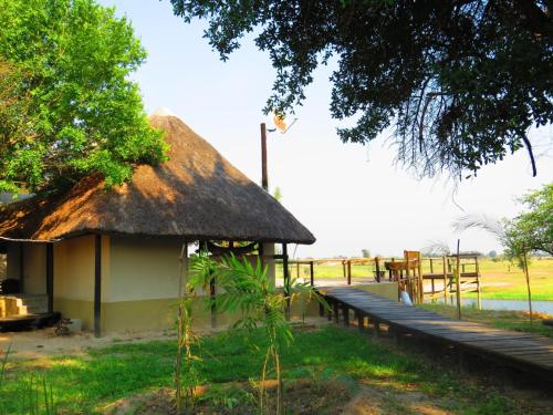 a hut with a thatched roof next to a field at Zambezi King Fisher Lodge in Katima Mulilo
