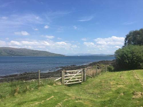 a wooden gate in a field next to a body of water at Alltcreich in Craignure
