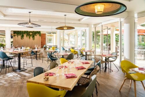 un restaurante con mesas, sillas y ventanas en Résidence Valdys Thalasso & Spa - les Pins, en Saint-Jean-de-Monts