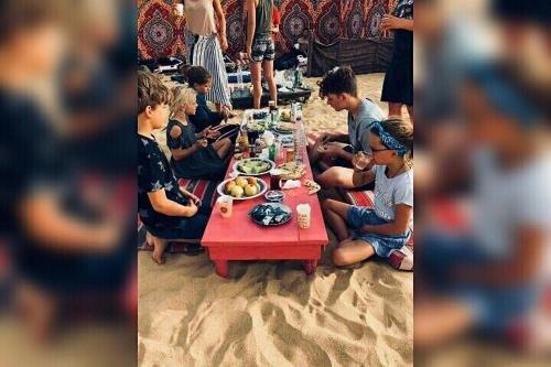 un grupo de niños sentados alrededor de una mesa comiendo comida en safari desert en Bawiti