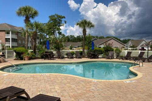 una piscina con mesas, sillas y palmeras en Cypress Bay 14-204, en Little River