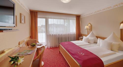 バート・フュッシンクにあるPension Maximilianのベッド、デスク、テレビが備わるホテルルームです。