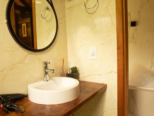 une salle de bain avec un lavabo blanc et un miroir dans l'établissement Chalé Canadense com Hidromassagem Pousada Índios Koroados, à Praia Grande