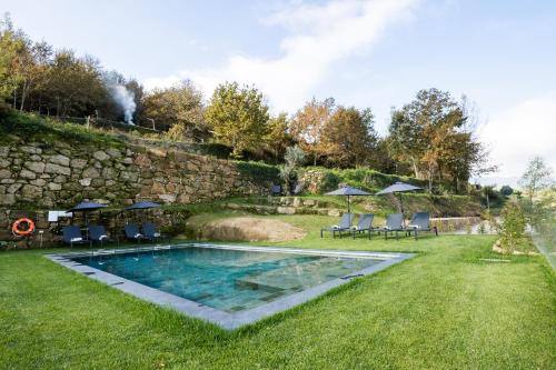 a pool in a yard with chairs and umbrellas at Douro Country House in Cinfães