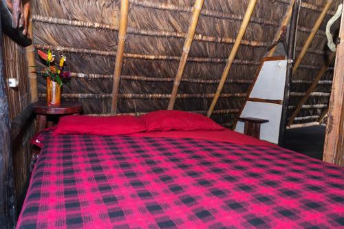 a red and black plaid bed in a thatched room at Magia Verde Lodge in Puerto Misahuallí