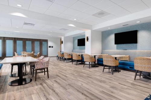 a waiting room with tables and chairs and a flat screen tv at Hampton Inn Chicago Orland Park in Orland Park