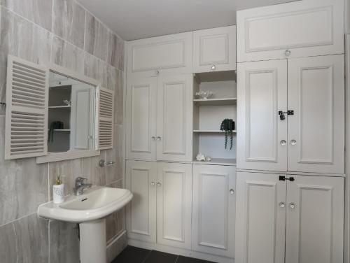 a white bathroom with a sink and white cabinets at Ty'n Lon in Penrhos-Lligwy