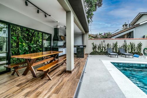 a patio with a wooden table and benches next to a swimming pool at Casa perfeita pro verão e inverno na Riviera in Bertioga