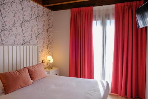 een slaapkamer met een bed met rode gordijnen en een raam bij Apartamentos & Wellnes LA QUIMERA DE AITANA Burgo de Osma in El Burgo de Osma