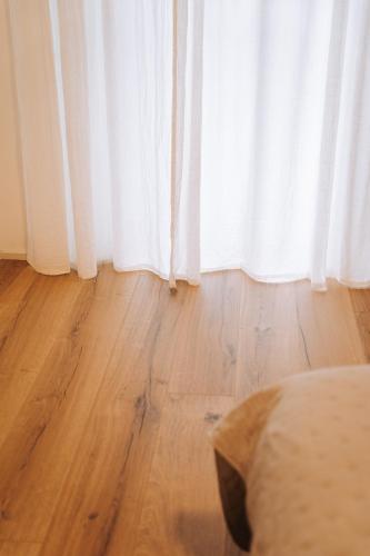 a bedroom with a wooden floor and a white curtain at Casa Camilla in San Michele allʼAdige