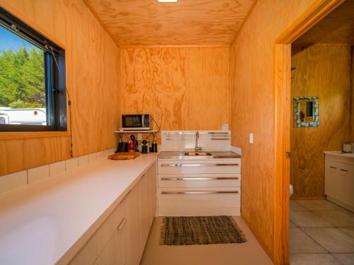a kitchen with wooden walls and white cabinets and a window at Whangapoua Hideaway - Whangapoua Bach in Whangapoua