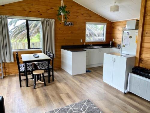 een keuken met witte apparatuur en een tafel met stoelen bij Relax Cabin - Waihi Beach Holiday Home in Waihi Beach