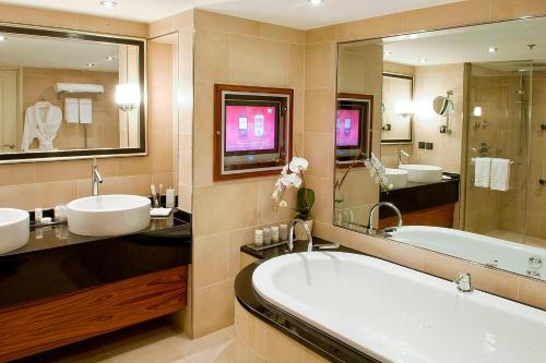 uma casa de banho com 2 lavatórios, uma banheira e um espelho grande em Paris Marriott Rive Gauche Hotel & Conference Center em Paris