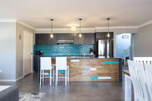 a kitchen with a counter with white chairs in it at Tipsy Turtle Beach House in Burrill Lake