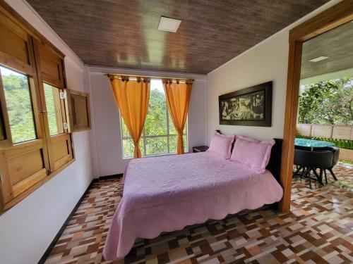 a bedroom with a bed with a purple comforter and two windows at Eco Hotel El Columpio in Salento