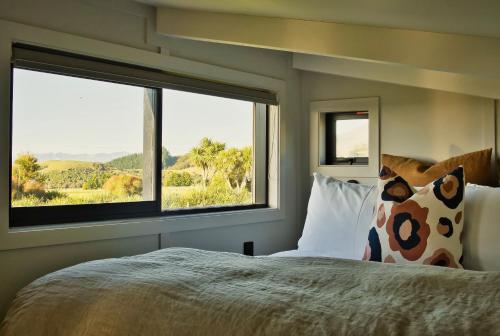 ein Schlafzimmer mit einem großen Bett und zwei Fenstern in der Unterkunft Kanuka Terrace - The Little Black House in Hapuku