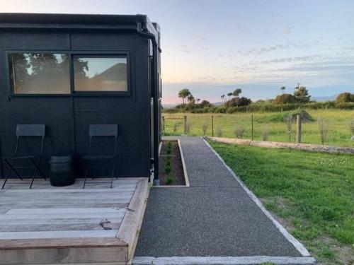 a black house with two chairs and a walkway at Kanuka Terrace - The Little Black House in Hapuku