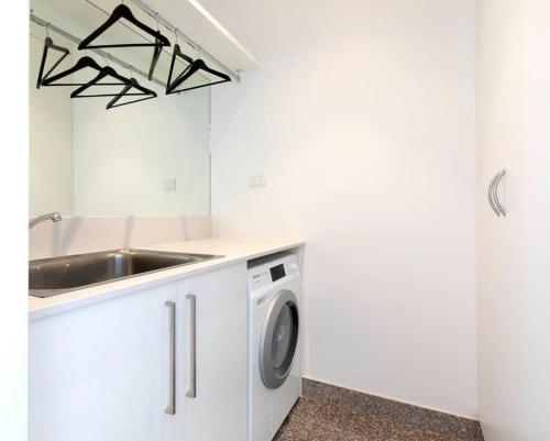 cocina blanca con fregadero y lavadora en SEA FOR MILES at Semaphore to relax & unwind, en Semaphore