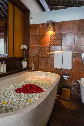 a bath tub filled with red flowers in a bathroom at Black Penny Villas Ubud in Ubud