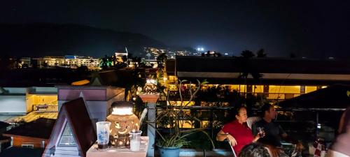 a couple of people sitting on a balcony at night at Kata Lina guesthouse in Kata Beach
