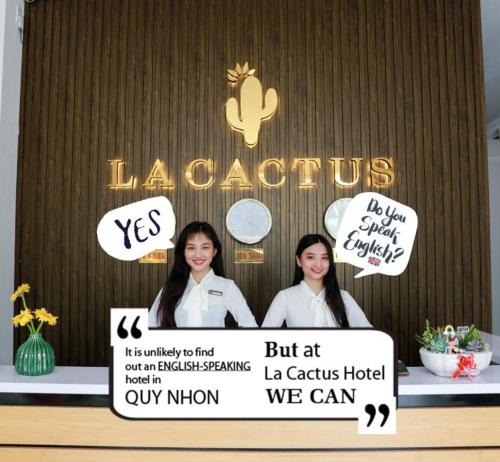 Due donne in piedi davanti a un cartello con dei cartelli di La Cactus Hotel 1 a Quy Nhon