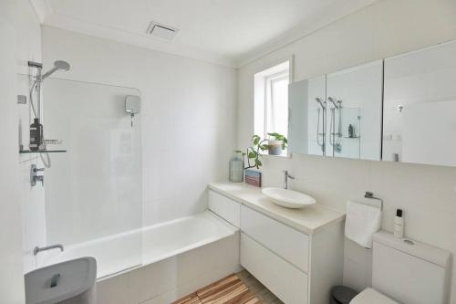 a white bathroom with a sink and a mirror at Beachfront Apartment on Bondi to Bronte Walk in Sydney