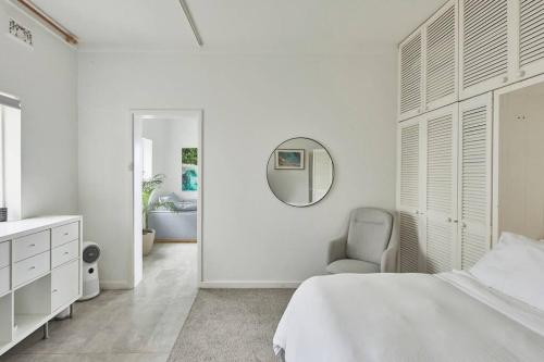 a white bedroom with a bed and a mirror at Beachfront Apartment on Bondi to Bronte Walk in Sydney