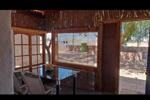 Habitación con mesa de cristal y 2 ventanas. en HOSTAL DON FELIX, en San Pedro de Atacama