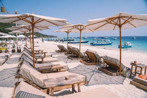 a beach with many chairs and umbrellas and the ocean at Gili Divers Hotel in Gili Trawangan