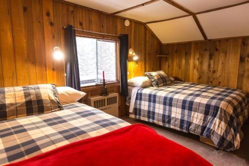 two beds in a room with wooden walls and a window at Red Shutter Inn in Rossland