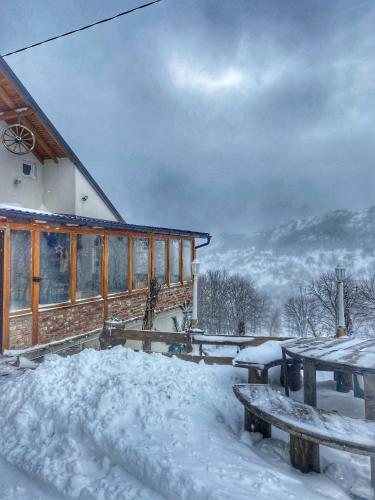 a house covered in snow with tables and benches at Konak Umoljani in Umoljani