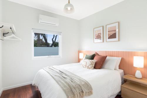 a white bedroom with a bed and a window at The Elements l Fire l 4 Stunning Apartments each with Private Outdoor Dining l Walk to the Beach l Family Friendly l Wifi l Netflix l Outdoor Shower l Communal BBQ Pavilion and Lawn Area l in Christies Beach