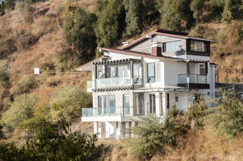 a white house on the side of a hill at Hostie Imperial Chalet-3 BHK Mountain Villa, Chail in Shimla