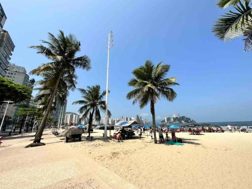 a beach with palm trees and people sitting on the sand at Apto 50m da praia Gonzaguinha São Vicente Edifício Estrela do Mar in São Vicente