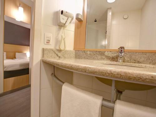a bathroom with a sink and a mirror and a bed at ibis Rio de Janeiro Barra da Tijuca in Rio de Janeiro