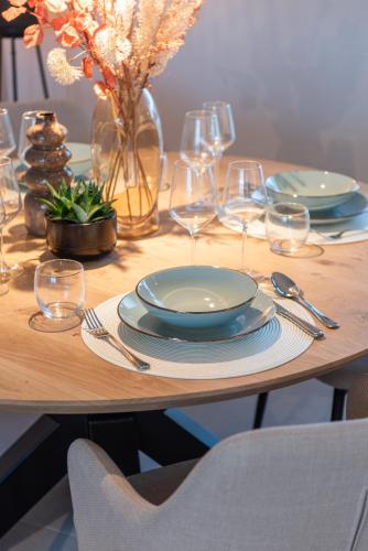 a wooden table with plates and wine glasses on it at NIEUW De Grenspaal ZUID 2slpk - 4P - SAUNA - LAADPAAL in Riemst
