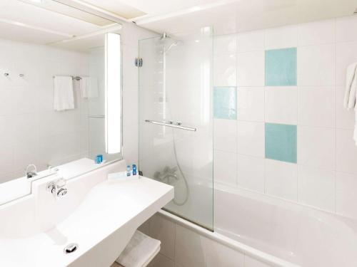 a white bathroom with a sink and a shower at Novotel Wien Hauptbahnhof in Vienna