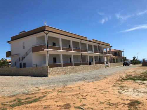 un grand bâtiment blanc sur un chemin de terre dans l'établissement ApartHotel Capo Rizzuto, à Ovile la Marinella