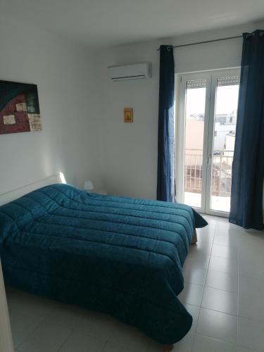 ein Schlafzimmer mit einem Bett mit blauer Decke und einem Fenster in der Unterkunft Casa del sole in Montalbano Ionico