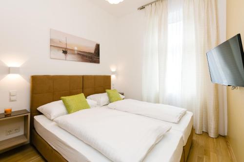 uma cama com lençóis brancos e almofadas verdes num quarto em Vienna Stay Apartments Castellez 1020 em Viena