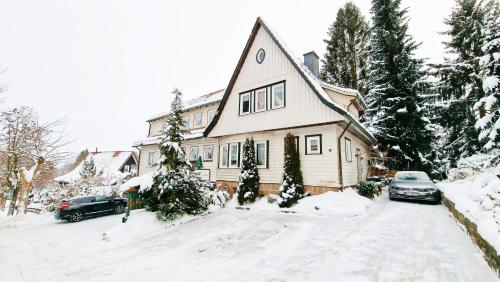 una casa nella neve con le auto parcheggiate nel vialetto di Hotel garni Am Hochwald a Braunlage