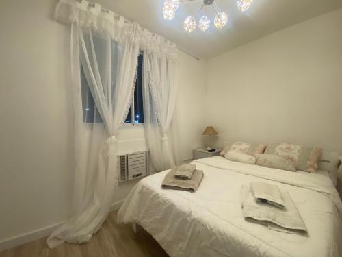 a white bedroom with a bed and a window at Conforto na Praia do Pontal in Rio de Janeiro