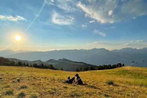 two people sitting on a grassy hill with the sun setting at Studio de la Marmotte - Aime 2000 in Aime La Plagne