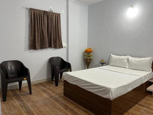 a bedroom with a bed and two black chairs at Lotus Guest House in Kharakvasla