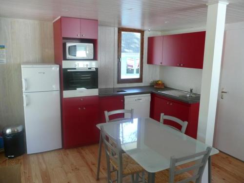 a kitchen with red cabinets and a table with chairs at Et pourquoi pas des vacances naturistes à la Jenny ? in Le Porge