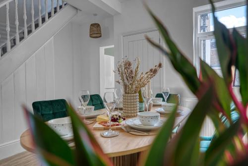 a dining room table with plates and glasses and a plant at Stunning Design 3-Bedroom Townhouse Retreat in Southsea, Sleeps 8, Chic and Spacious with Free Parking Permit, SPRING SPECIAL OFFER AVAILABLE! - by Blue Puffin Stays in Portsmouth