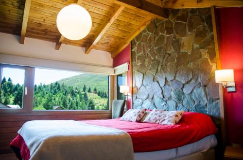 1 dormitorio con pared de piedra y 1 cama con sábanas rojas en Apartamentos Catedral Inn en San Carlos de Bariloche