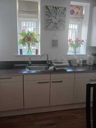 a kitchen with white cabinets and a sink and two windows at BODLONDEB CASTLE BED & BREAKFAST { CENTRAL LLANDUDNO} in Llandudno