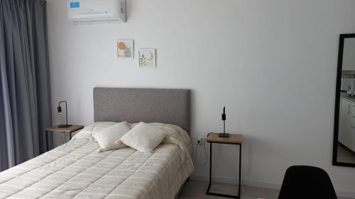 ein Schlafzimmer mit einem weißen Bett mit 2 Tischen und einem Spiegel in der Unterkunft Departamento 57 Parque San Martin in La Plata