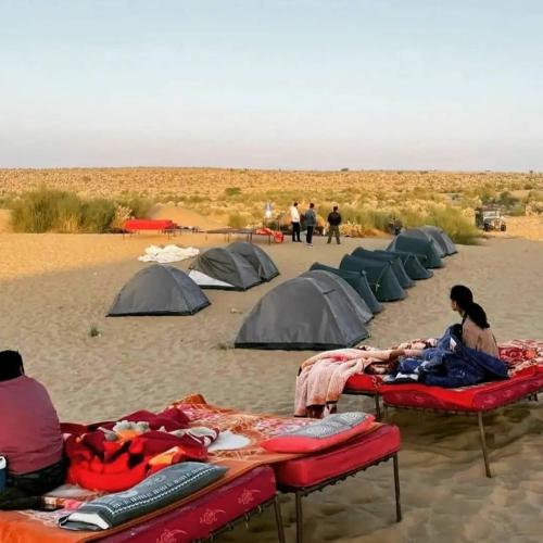 a group of tents in the desert with people standing around at Mirvana Guest House & Camel safari in Jaisalmer